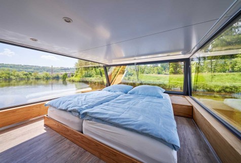 The upper sleeping area is a special highlight of the houseboat: here you can start the day with a panoramic view, enjoy breakfast in bed with a view of the water, or watch nature at night. The window can simply be tilted inwards to let in fresh air. Foto: Studio Blickfang